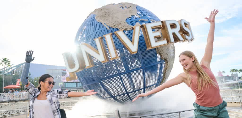 Two women enjoy a fun moment in front of a large Universal globe sculpture at a theme park during daytime