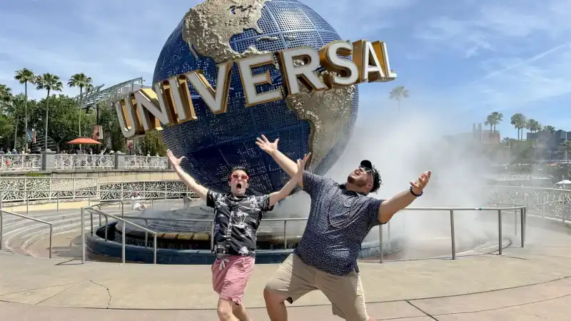 Two friends throwing their arms up in excitement in front of the Universal globe fountain at Universal Orlando Resort.