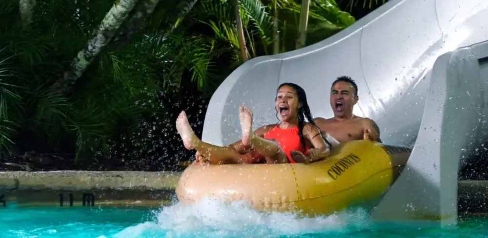 Two children are enjoying a ride on a
                                  yellow water slide into a pool at a water park.