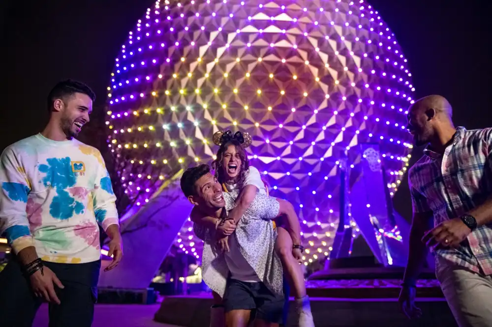 Friends laugh together as Spaceship Earth glows purple and gold behind them during an after-hours evening at EPCOT.