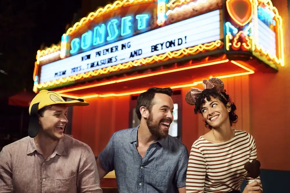Three friends laughing together beneath the glowing Sunset Boulevard marquee at Disney's Hollywood Studios during an after-hours evening.