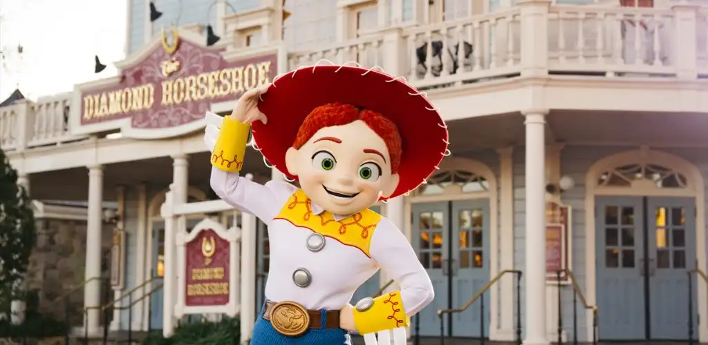 A cheerful cowboy character in a white shirt, yellow accents, and a red hat stands in front of a vintage-style building with a sign that reads Diamond Horseshoe.
