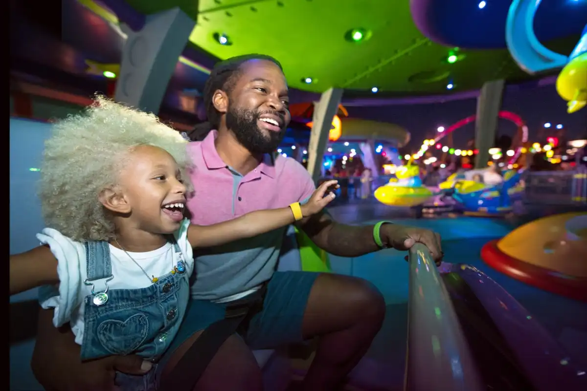 A father and daughter grin as they spin through the neon-lit Alien Swirling Saucers attraction at Disney's Hollywood Studios after dark.
