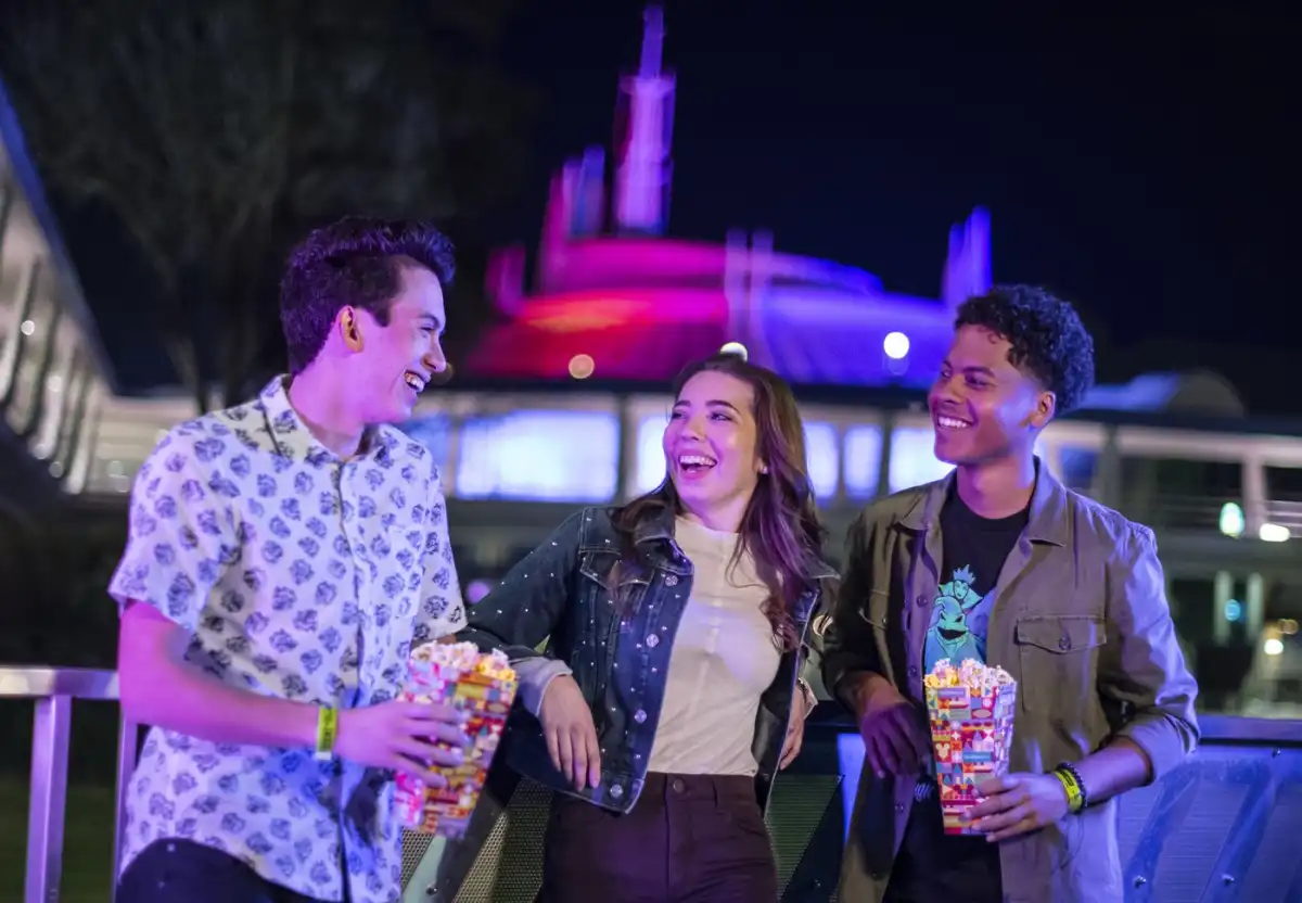 Three friends share popcorn beneath the illuminated peaks of Space Mountain at Magic Kingdom Park during an after-hours event.