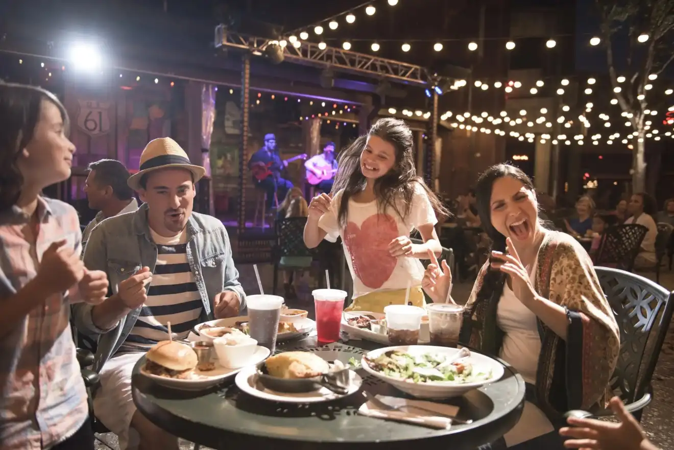 Family enjoying a lively dining experience at Disney Springs, savoring delicious food with live music and twinkling string lights creating a vibrant atmosphere 
