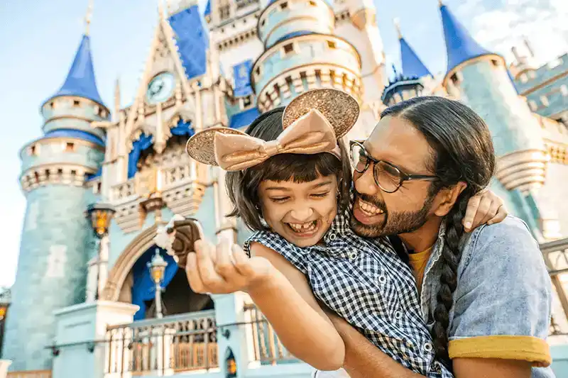 Father and daughter sharing a magical moment in front of Cinderella Castle at Magic Kingdom Park, smiling while enjoying a sweet treat