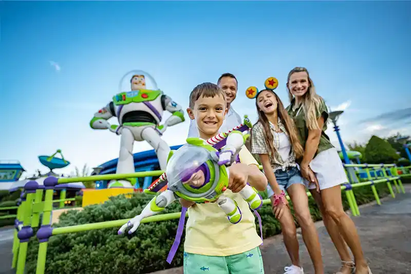 Excited child holding a Buzz Lightyear toy with family at Toy Story Land in Disney’s Hollywood Studios, featuring a larger-than-life Buzz Lightyear statue.