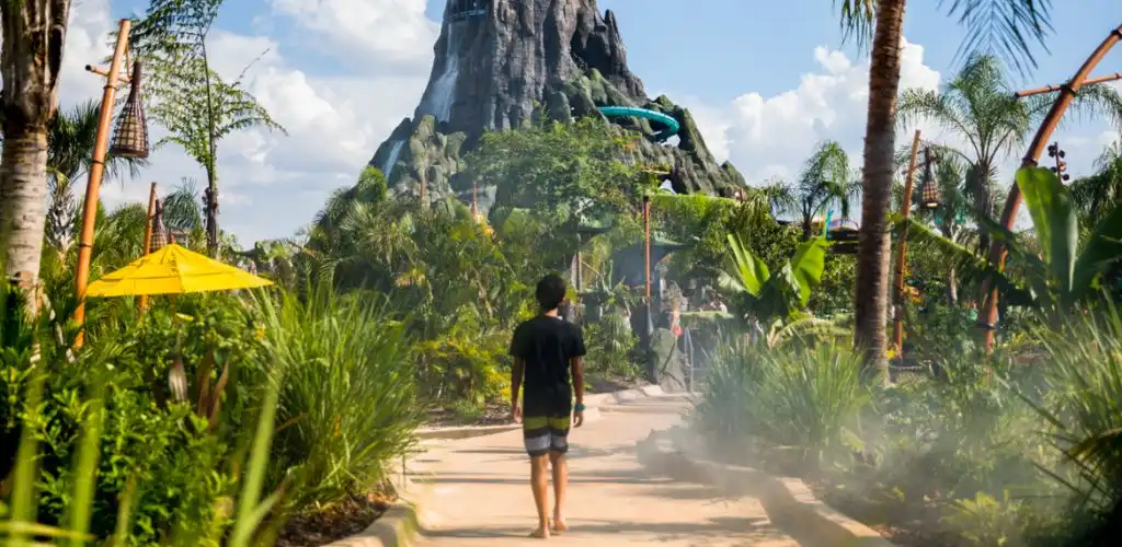 Guest walking through lush tropical pathways at Universal’s Volcano Bay, approaching the towering Krakatau volcano surrounded by water slides and island-themed scenery.