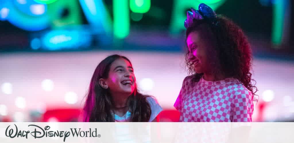 Two young girls laughing and enjoying themselves under colorful neon lights at Magic Kingdom Park during the Disney After Hours even
