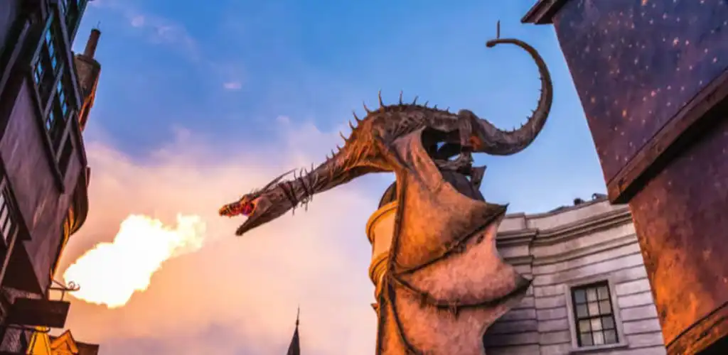 Fire-breathing dragon perched atop a building at Universal Studios Florida, roaring with flames against a stunning sunset sky.