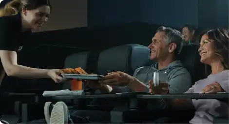 A women serves food to a men and women seated in a movie theater, creating a friendly and inviting atmosphere.