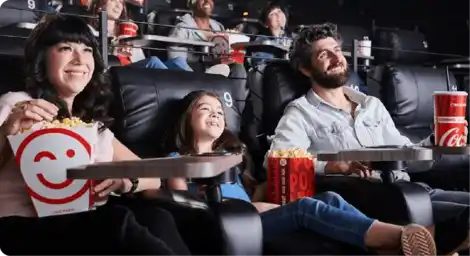 A happy family enjoying popcorn together in a movie theater, all smiling as they watch the film.