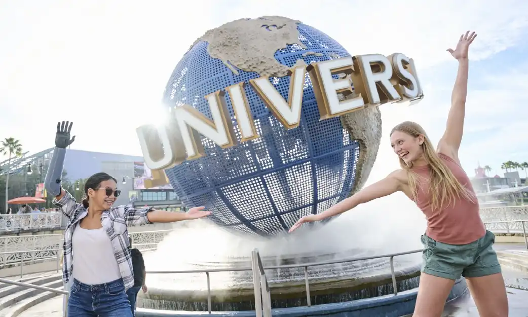 Two friends striking playful poses in front of the iconic Universal globe at Universal Orlando Resort, capturing the excitement of their visit.