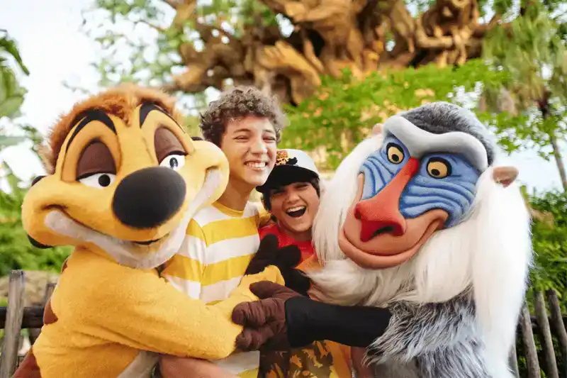 Guests laughing and posing with Timon and Rafiki at Disney's Animal Kingdom, with the Tree of Life in the background
