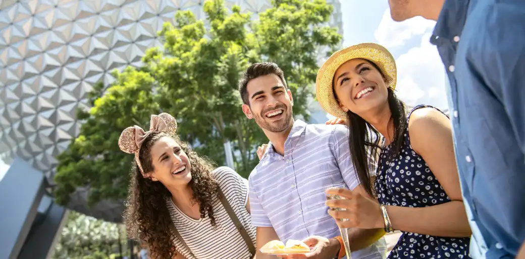 Group of diverse friends smiling and enjoying outdoors during daytime with modern architecture and green trees in background