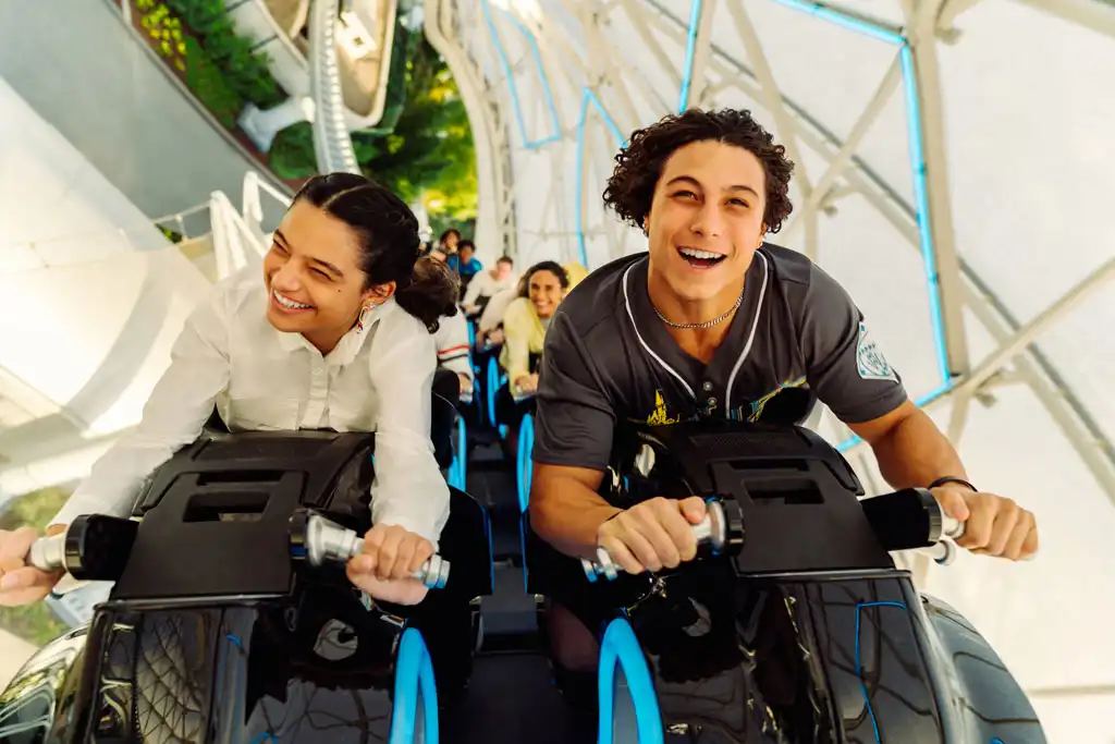 Two people in wheelchairs enjoying a thrill ride at a theme park smiling and having fun while riding together.