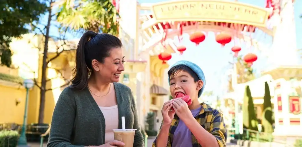A woman and boy enjoying food outdoors at a festive location with colorful decorations and an entrance archway.