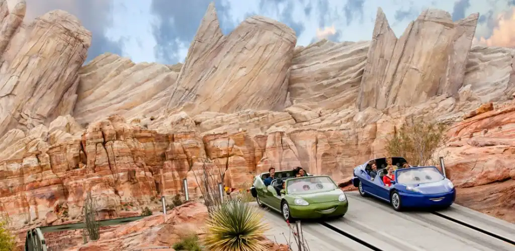 People riding futuristic themed roller coaster cars through a desert canyon landscape with rocky formations and sparse vegetation