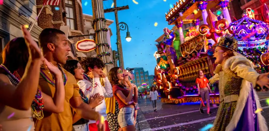 A parade float with colorful lights and decorations passes by on a city street during a celebration with people watching and wearing festive accessories.