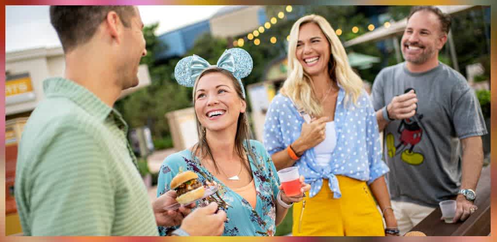 Group of friends enjoying outdoor drinks and food at a festive gathering with string lights and cheerful expressions
