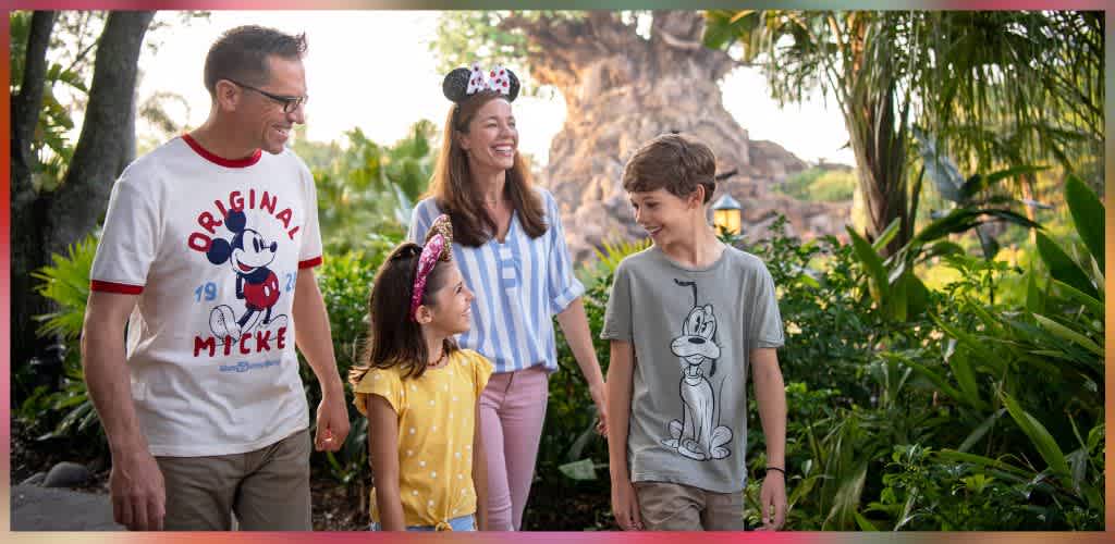 A smiling family of four walking outdoors among lush greenery and trees, enjoying a sunny day together.