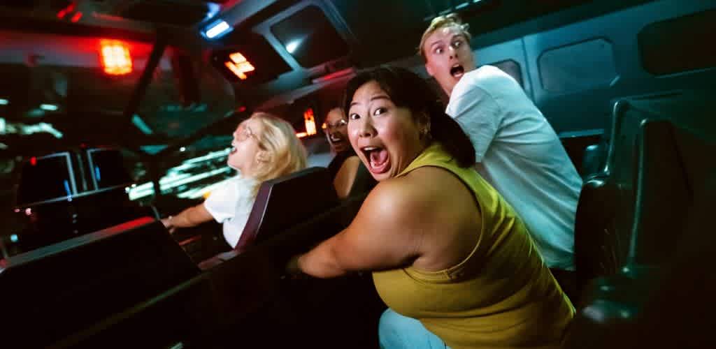 Four excited women experiencing fun and thrill in a roller coaster at an amusement park at night