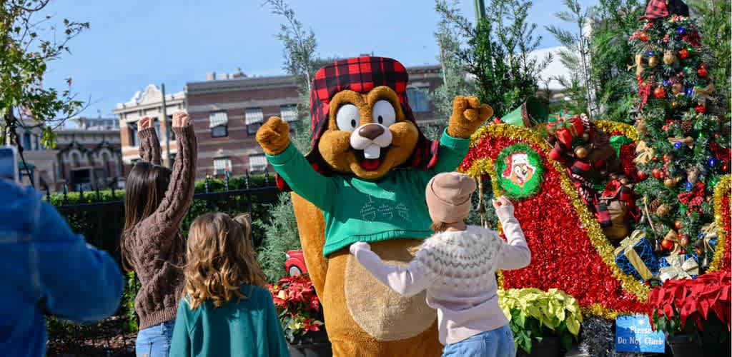 A person in a lion mascot costume wearing a holiday hat and green sweater interacts with children near a decorated Christmas tree outdoors.
