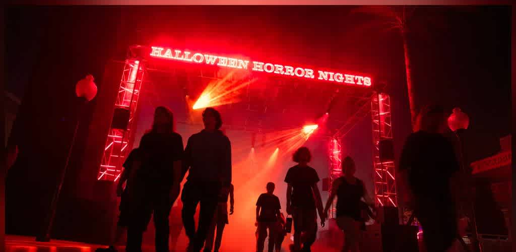 People walking through a haunted house with red lighting and a sign reading Halloween Horror Nights at the entrance