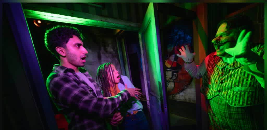 People surprised and scared by a colorful haunted house clown acting with hands raised and a wide smile