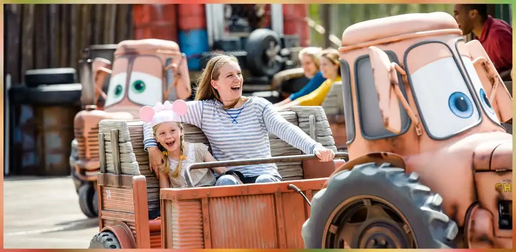 Smiling children enjoy riding a tractor-themed amusement park ride with clown faces and colorful background activity.