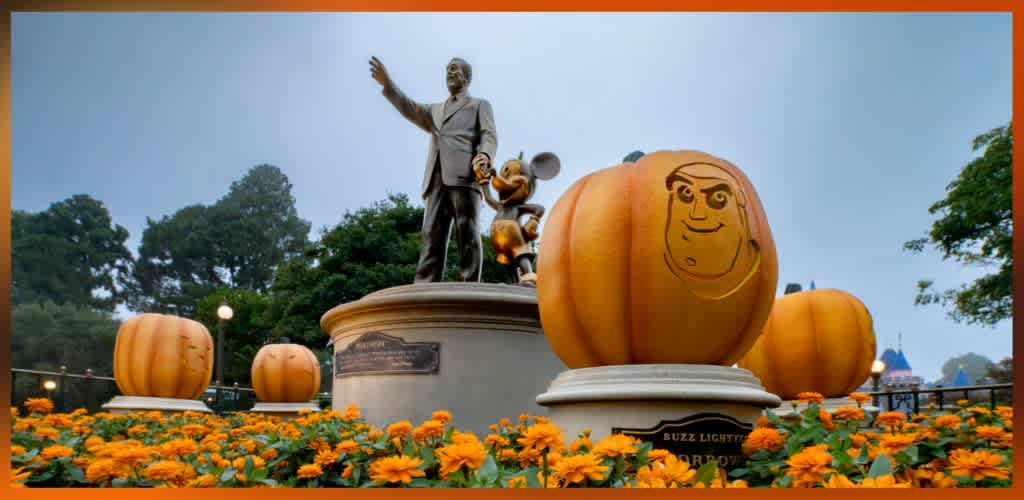 Statue of Walt Disney with Mickey Mouse surrounded by large carved pumpkins and orange flowers in a festive outdoor setting