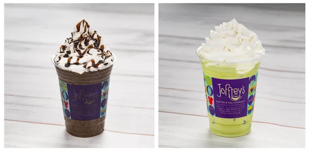Two colorful coffee beverages topped with whipped cream and chocolate or caramel drizzle on a white wooden surface
