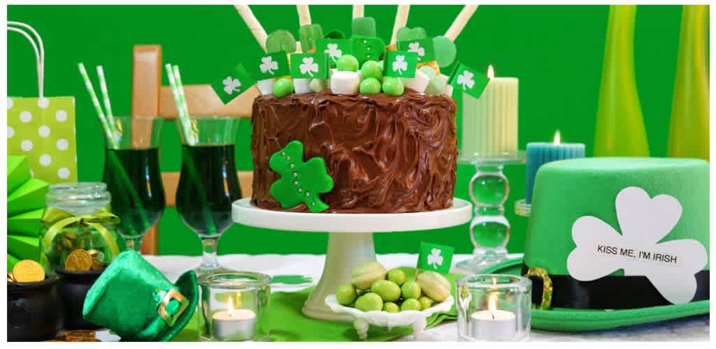 A festive Saint Patrick's Day celebration features a chocolate cake with shamrock decorations, green drinks, candles, and green-themed party accessories.