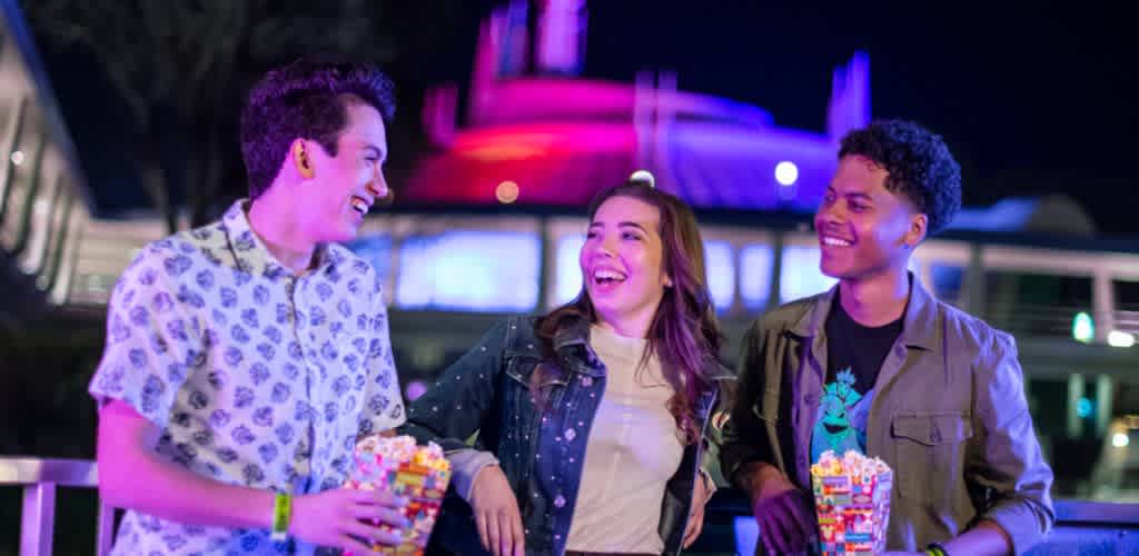 Three young adults smiling and holding colorful toys at night in an outdoor setting with vibrant neon lights
