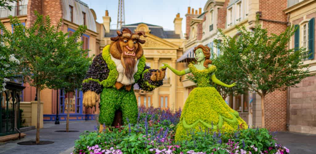 Colorful topiary sculptures of Beauty and the Beast characters located outdoors on a city street with trees and flowers