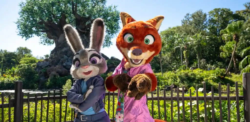 People in bunny and fox costumes posing outdoors in front of a tree and greenery on a sunny day