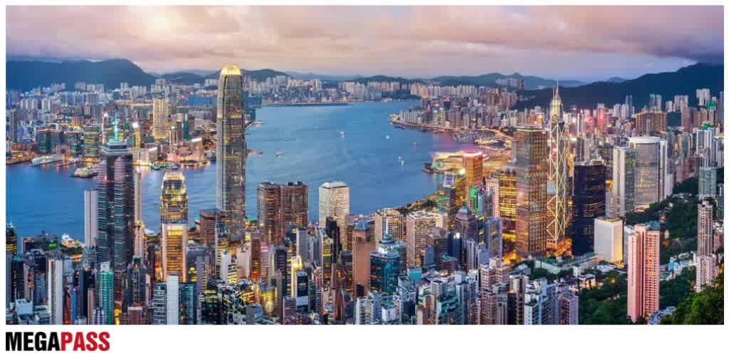 Aerial view of a vibrant city skyline at dusk with tall buildings, a river, and mountains in the background.