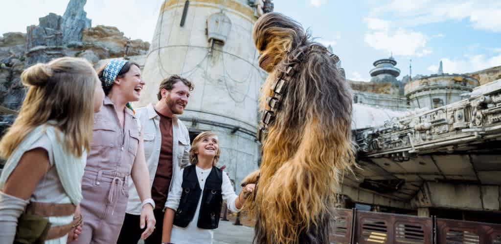 A group of people and a large Chewbacca costume character enjoying a themed outdoor location with buildings and a cloudy sky in the background