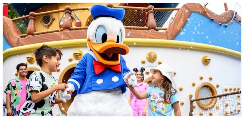 Children and adults enjoying a Disney characters featuring Mickey Mouse and a large Donald Duck mascot outdoors at a themed amusement park