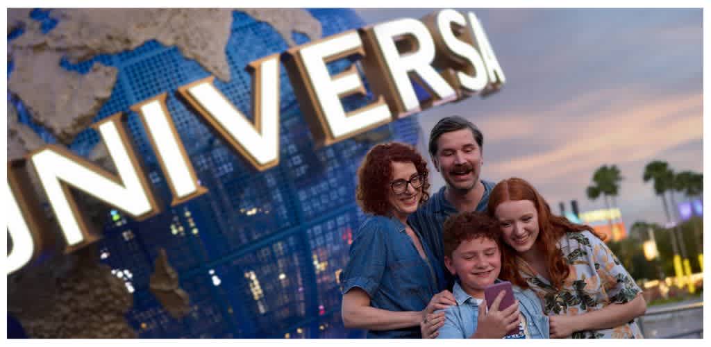A happy family of four taking a selfie in front of a Universal Studios sign at sunset