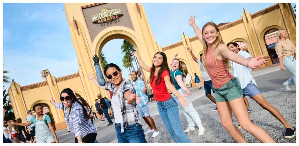 Group of diverse people smiling and dancing outside the Universal Studios Florida entrance on a sunny day