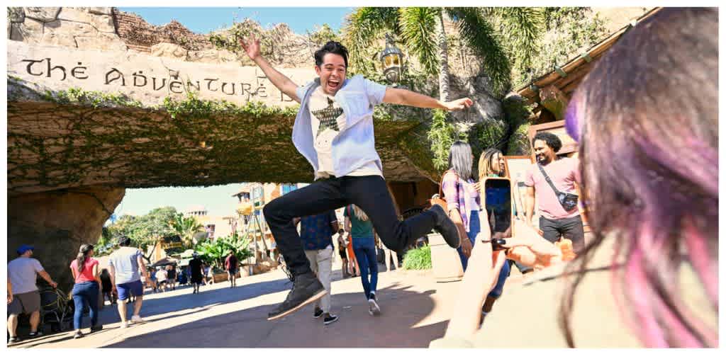Young man jumping excitedly while people watch and take photos in an amusement park setting