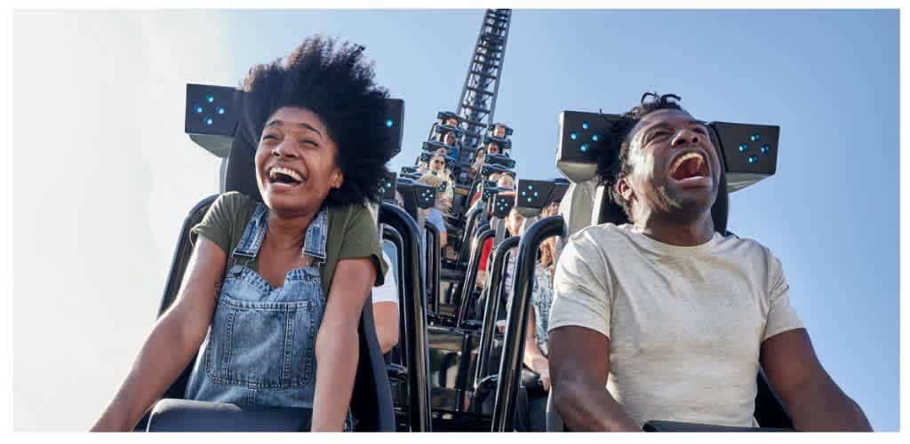 Two people experiencing joy on a roller coaster ride during daytime at an amusement park