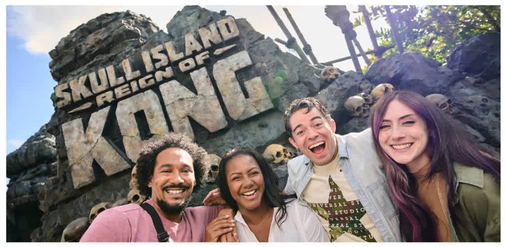 Group of diverse friends smiling outdoors at Skull Island Reign of Kong attraction with rocks and skull decorations in the background