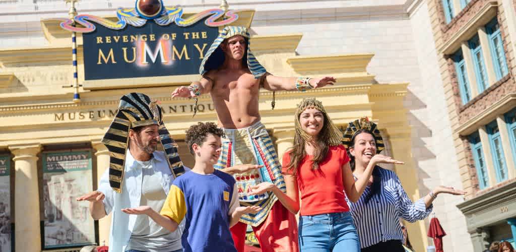 Group of people dressed as ancient Egyptians performing a show in front of a museum entrance with a sign reading Revenge of the Mummy and Museum Antiques