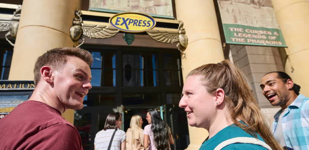 People smiling and talking outside the entrance of a themed amusement park with a sign that says EXPRESS above the door