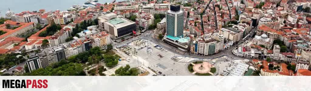 Aerial view of a city with tall buildings, a large plaza, and green trees surrounding urban structures.