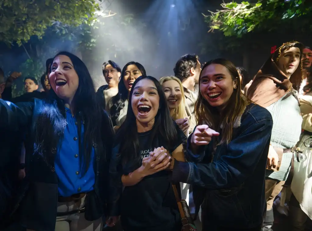 Group of diverse people smiling and enjoying an event under colorful lighting and trees outdoors