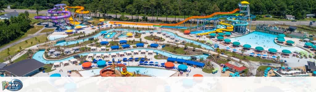 An aerial view of a large water park with multiple colorful water slides, lazy rivers, splash pools, and shaded lounging areas.