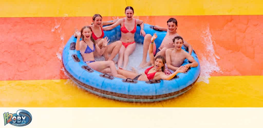 Six people are enjoying riding an inflatable water tube on a colorful water slide at a water park.